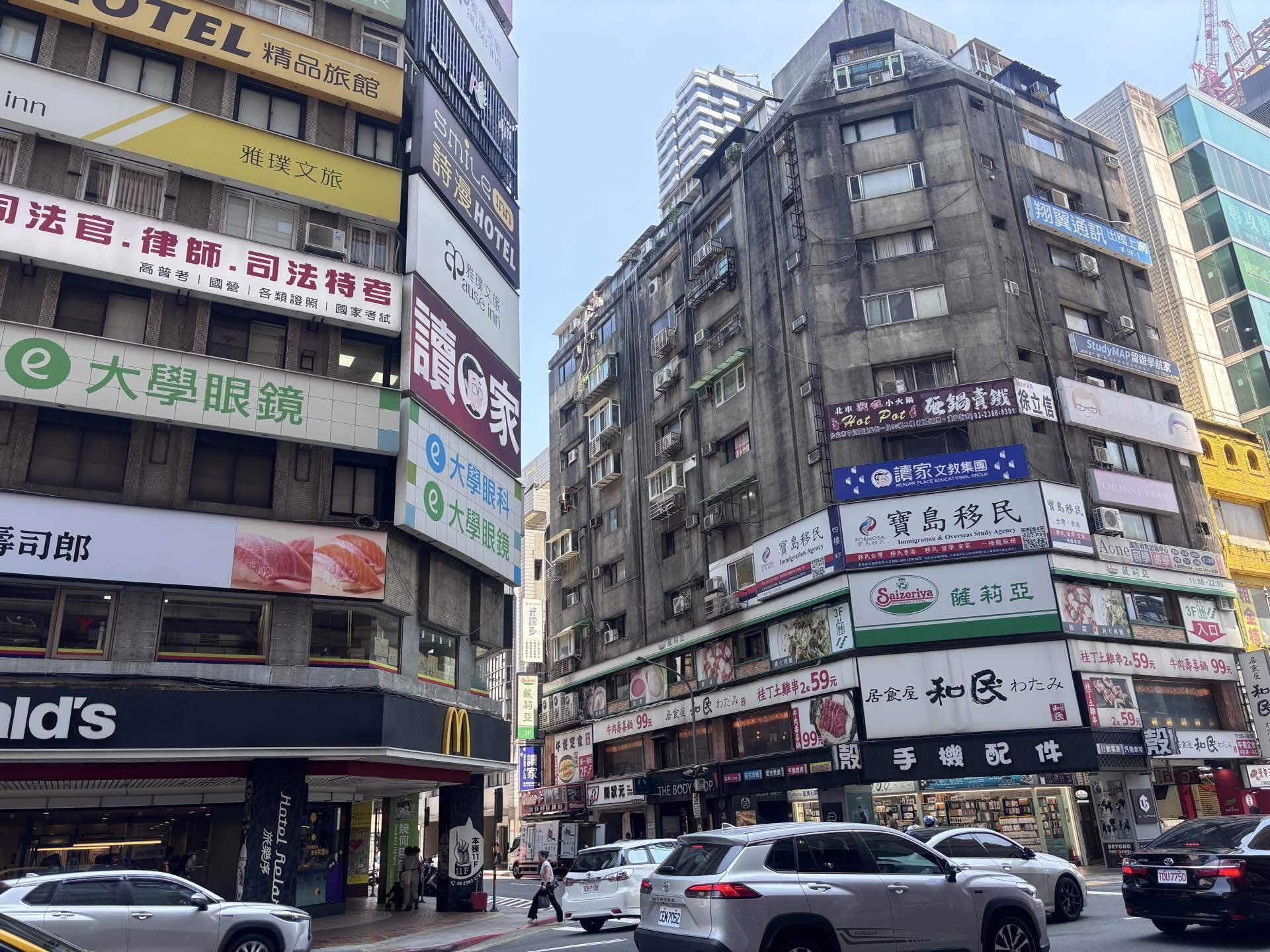 晴天の台北市街の交差点。看板が並ぶビル街を歩く観光客